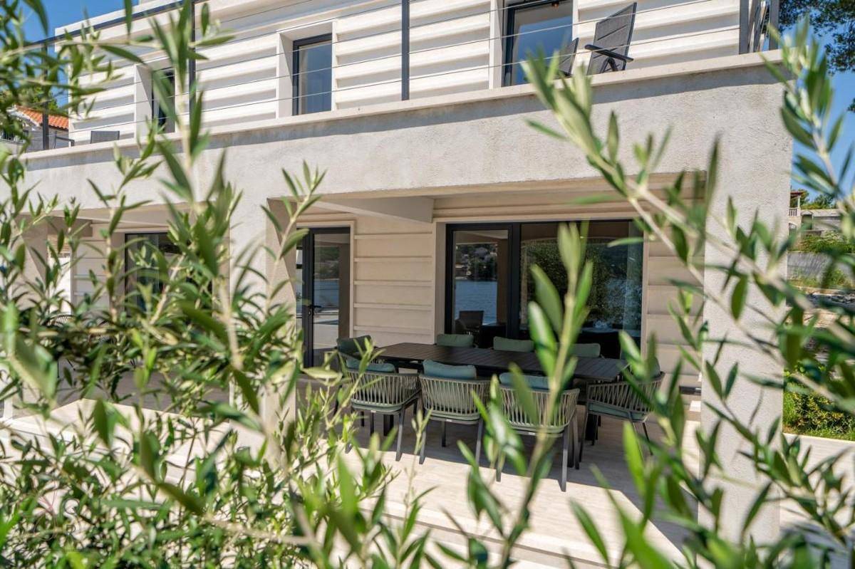 Geräumige überdachte Terrasse mit Esstisch und Stühlen, umgeben von mediterraner Vegetation.