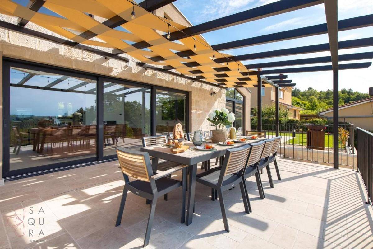 Überdachte Terrasse mit großem Esstisch und Zugang zum Innenbereich durch Glasschiebetüren.
