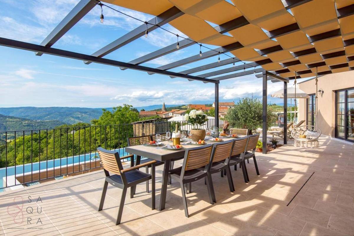 Geräumige Terrasse mit Esstisch unter einer Pergola und weitem Blick über die Landschaft.