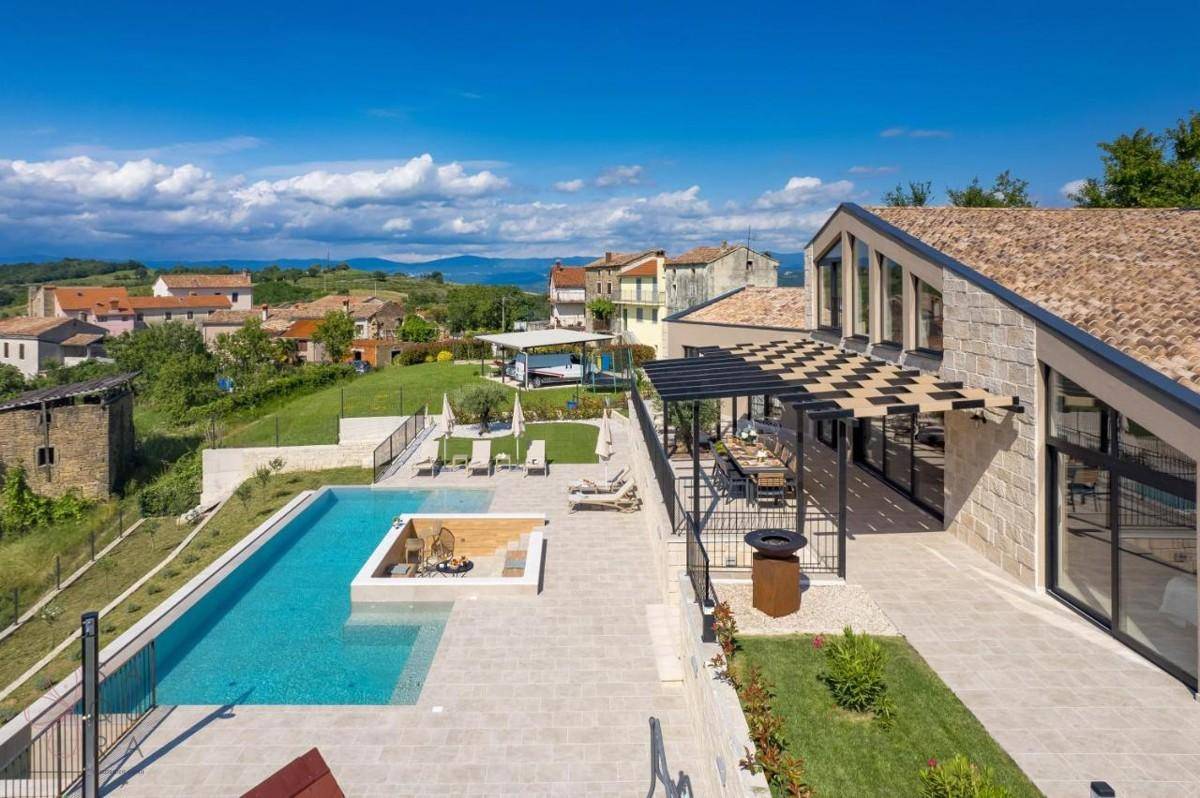 Weitläufige Außenanlage einer modernen Villa mit Pool, Liegebereich und Blick auf das Dorf.