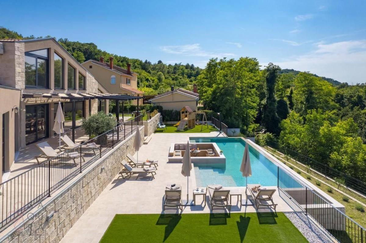 Seitlicher Blick auf die Villa mit weitläufiger Poolterrasse und Liegestühlen unter Sonnenschirmen.