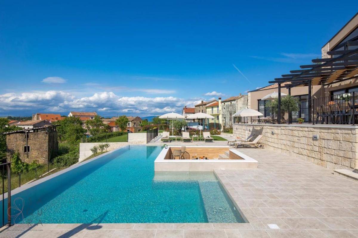 Weitläufiger Poolbereich mit Infinity-Pool, Liegestühlen und Blick auf das charmante Dorf.