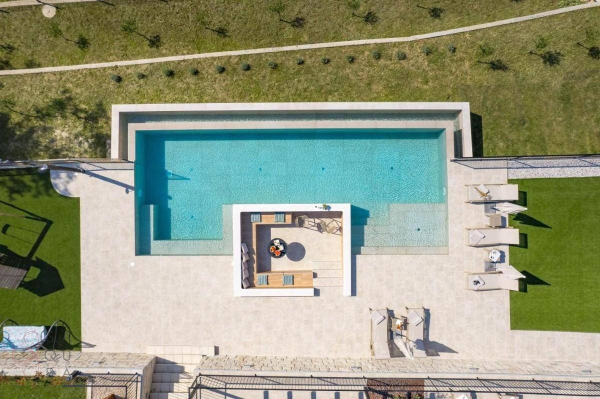 Vogelperspektive des Pools mit integrierter Lounge und Liegebereich auf Kunstrasen.