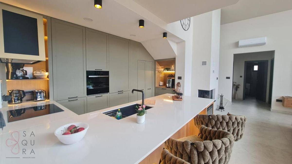 Moderne Küche mit heller Arbeitsplatte, integrierten Geräten und einer Kücheninsel mit Barhockern.