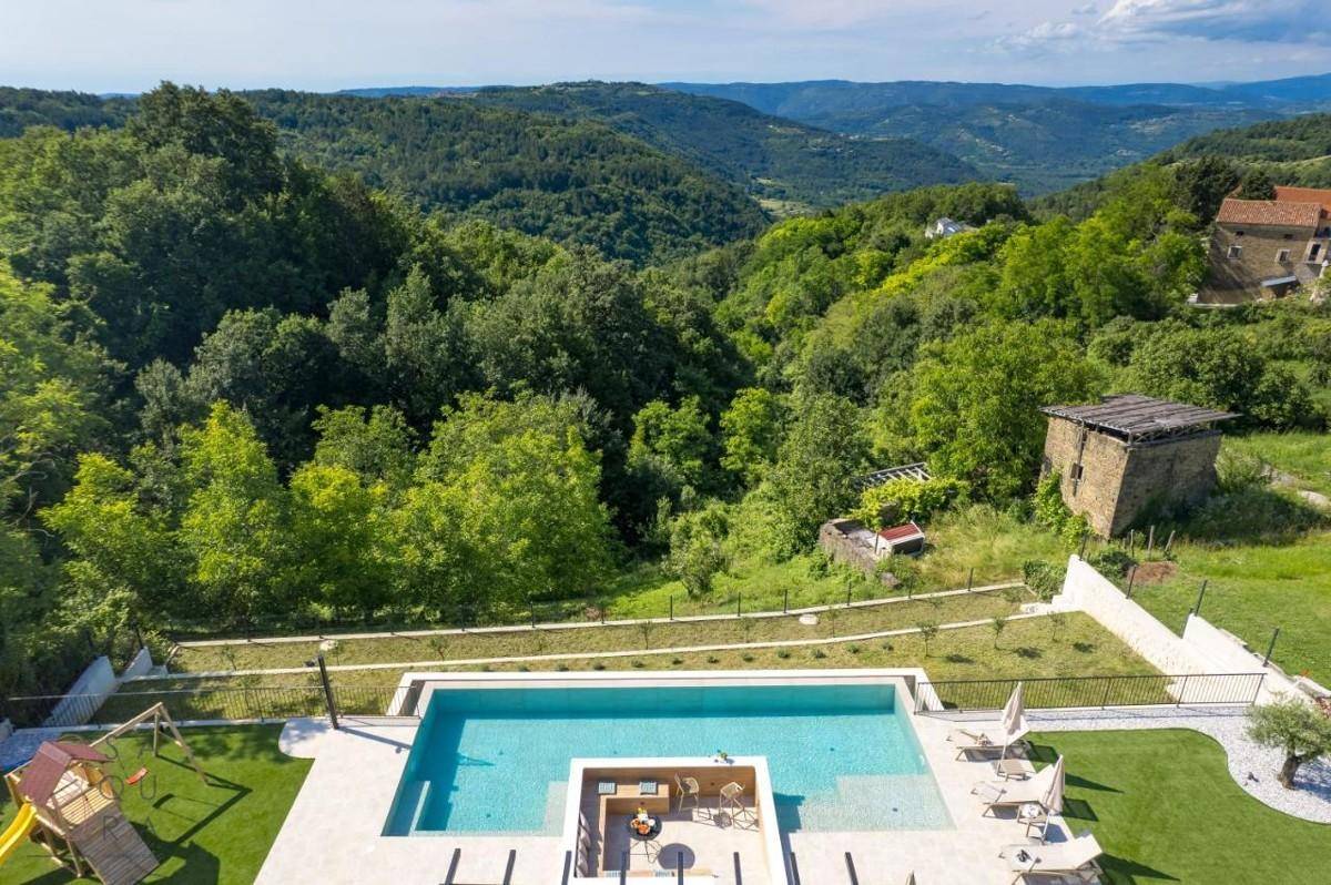 Vogelperspektive des Pools mit Liegebereich, Kinderspielplatz und weitem Blick über die grüne Landschaft.