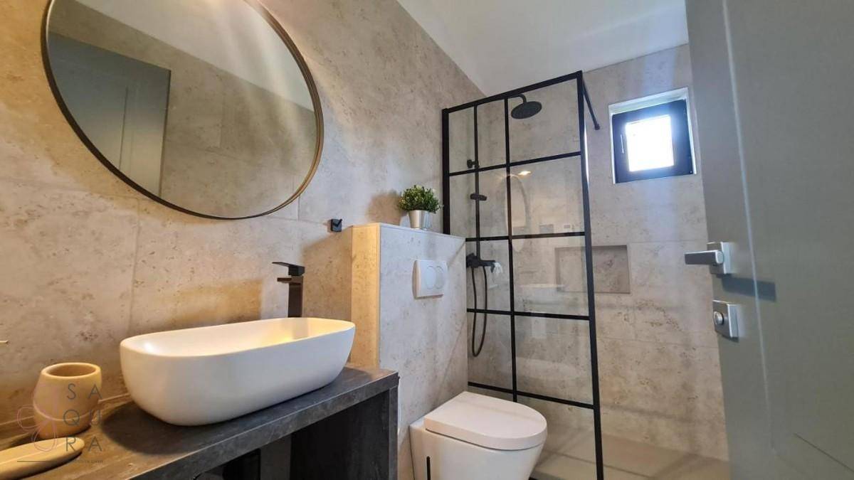 Modernes Badezimmer mit Aufsatzwaschbecken, wandhängendem WC und einer begehbaren Dusche mit schwarzem Rahmen.