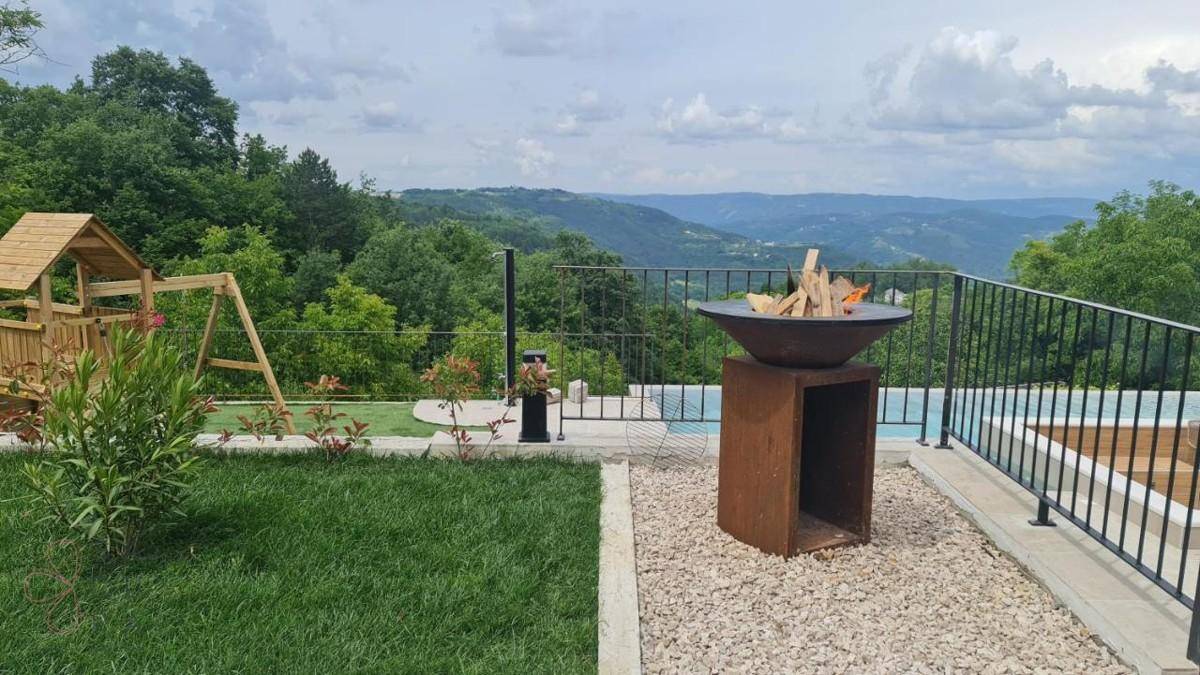 Großer Gartenbereich mit Feuerstelle, Kinderspielplatz und Infinity-Pool mit weitem Blick auf die grüne Landschaft.