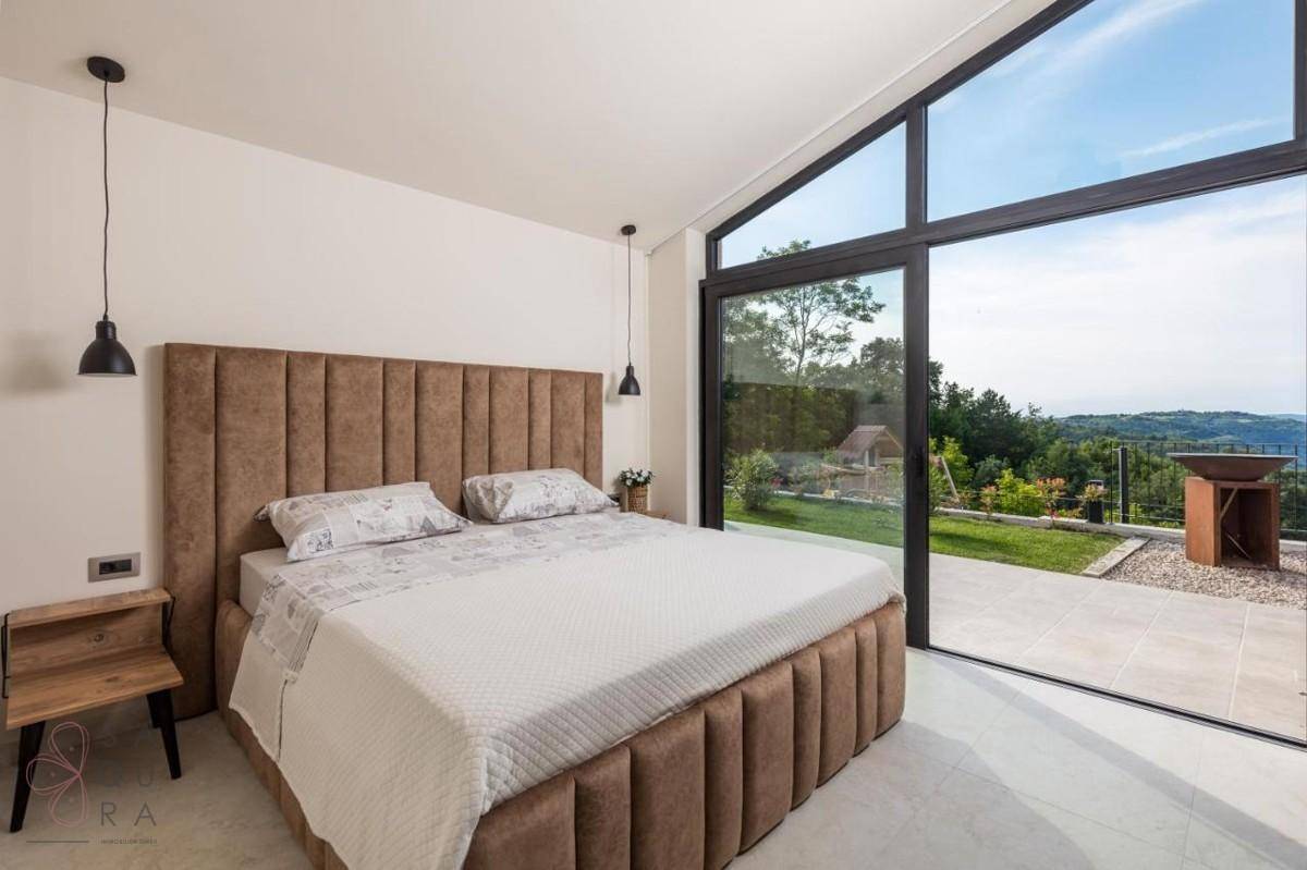 Modernes Schlafzimmer mit großem Bett und raumhohen Fenstern, die einen weiten Blick ins Grüne bieten.