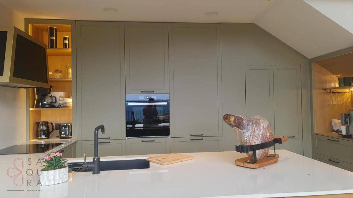 Detailansicht der modernen Einbauküche mit hellgrünen Schränken, Induktionskochfeld und integriertem Backofen.