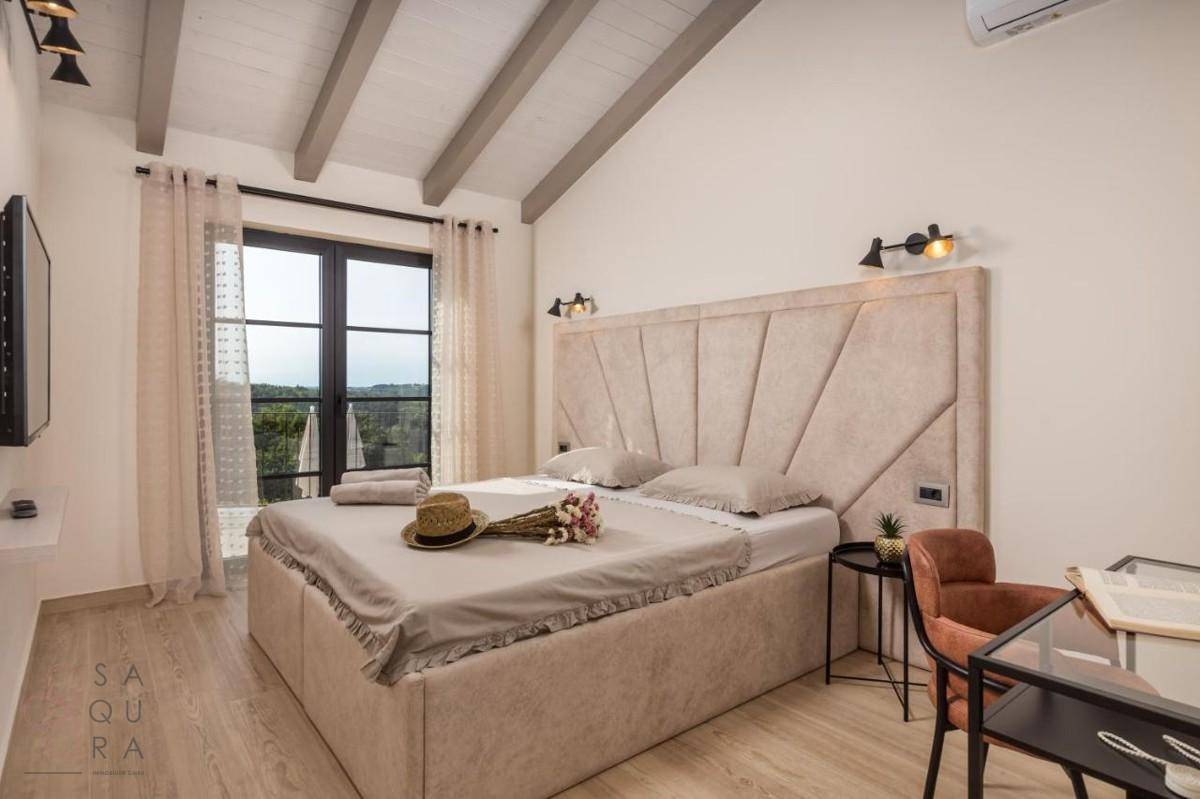 Helles Schlafzimmer mit großem Bett, sichtbaren Deckenbalken und Zugang zu einem Außenbereich.