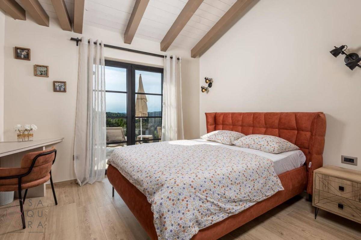 Komfortables Schlafzimmer mit orangefarbenem Bett, Holzbalkendecke und Zugang zu einem sonnigen Balkon.