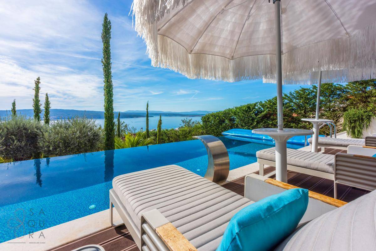 Sonnenliegen am Infinity-Pool mit weitem Meerblick unter strahlend blauem Himmel.
