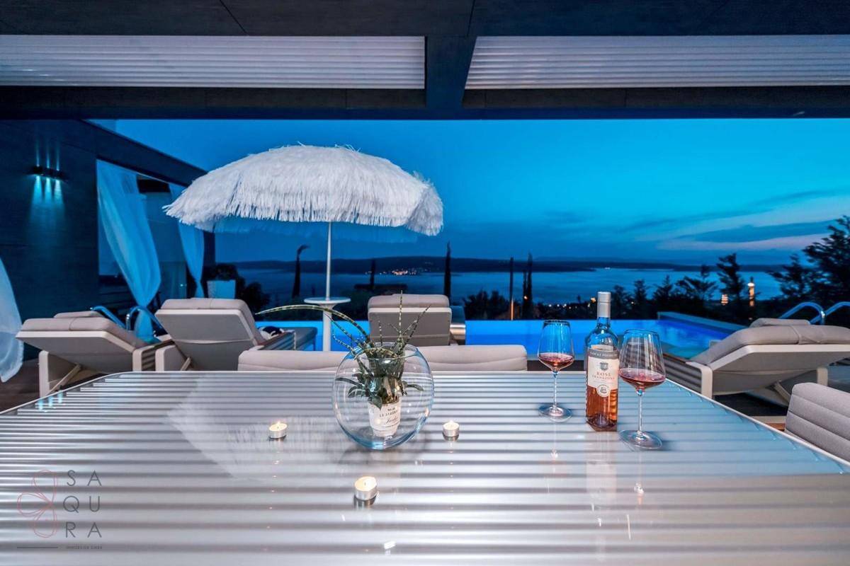 Gemütlicher Essbereich im Freien auf der Terrasse mit Pool und malerischem Meerblick in der Dämmerung.