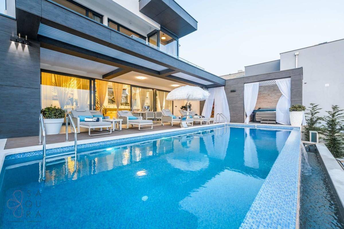 Luxuriöse Villa mit großem Pool und weitläufiger Terrasse, umgeben von mediterraner Vegetation.