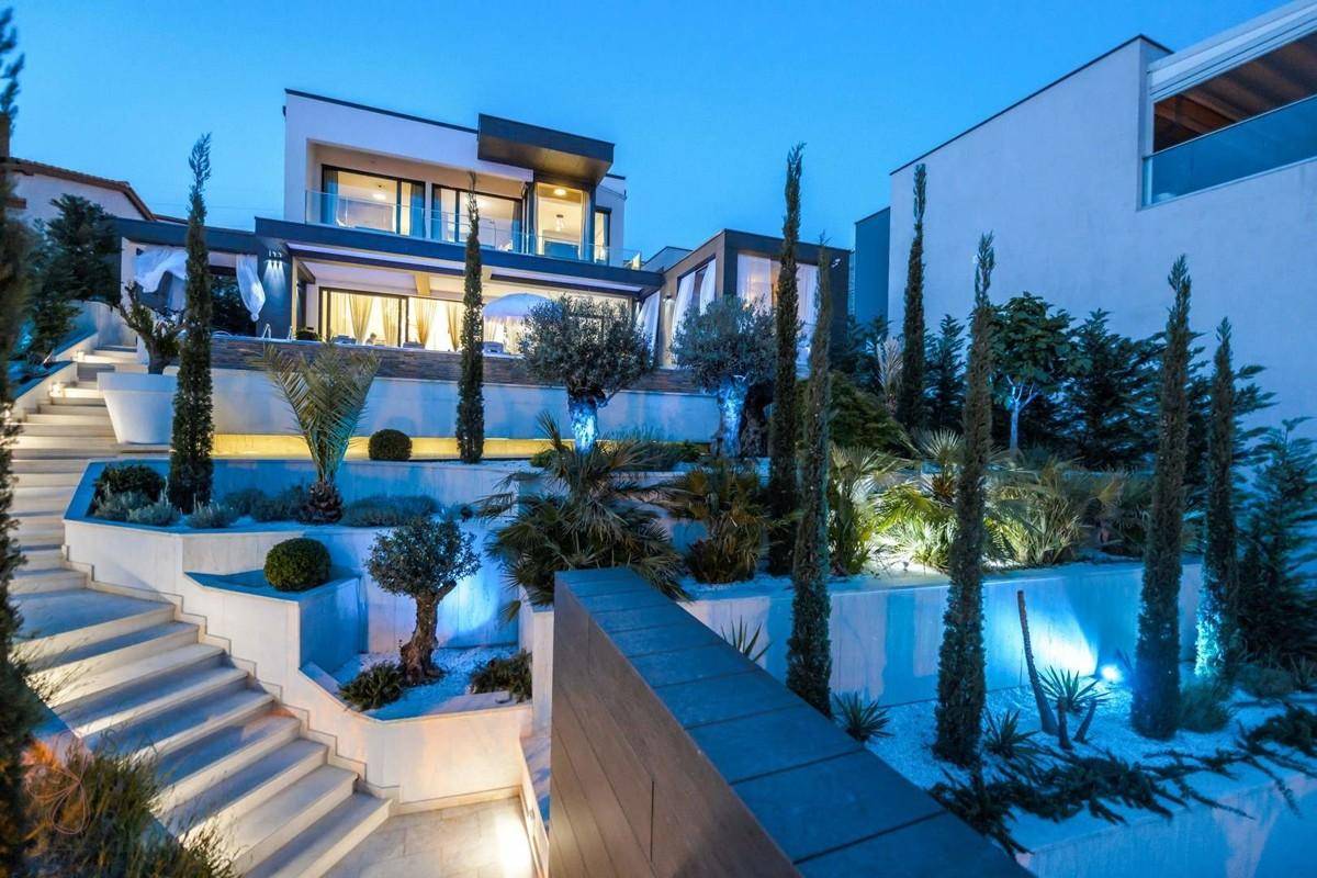 Luxuriöse Villa mit beleuchtetem Garten und stilvoller Architektur in der Abenddämmerung.