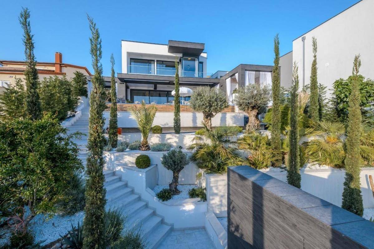 Elegante moderne Villa mit gestuftem Garten und mediterraner Bepflanzung unter blauem Himmel.