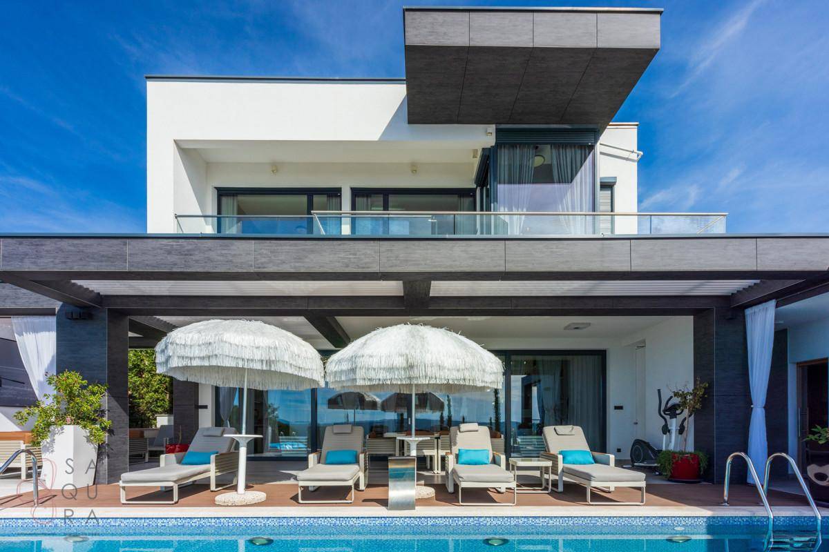Außenbereich der Villa mit großem Pool, Sonnenliegen und Blick auf das Meer.