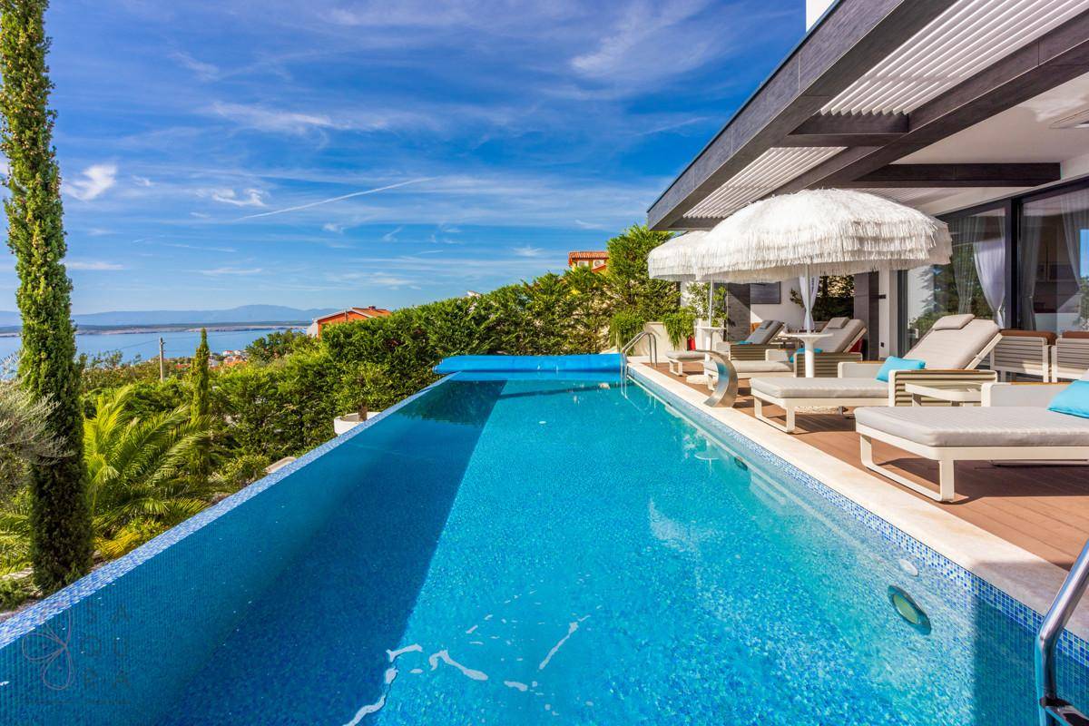 Langer Infinity-Pool mit blauen Mosaikfliesen und weitem Blick auf das Meer und die Küste.