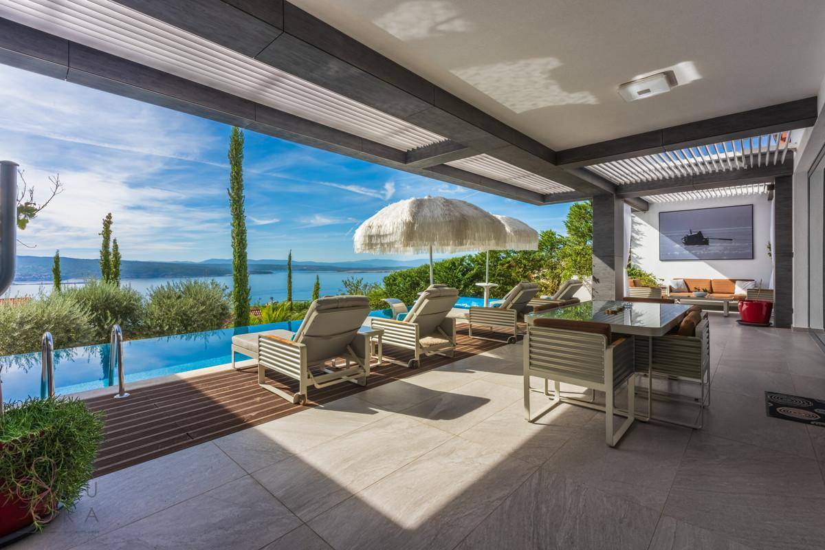 Geräumige Terrasse mit Essbereich und Sonnenliegen am Pool mit Panoramablick auf das Meer.