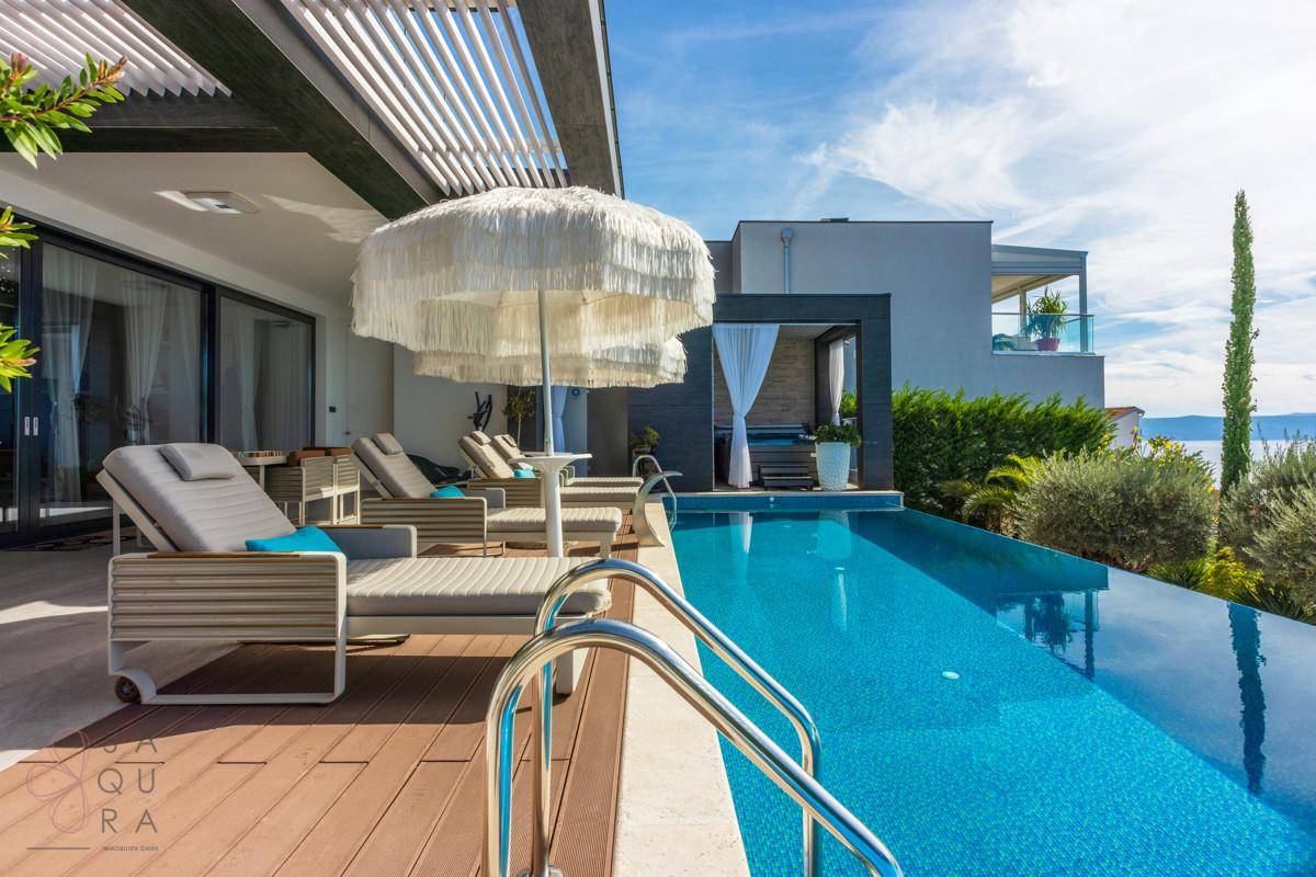 Sonnenliegen am Pool mit Blick auf das Meer und die moderne Architektur der Villa.