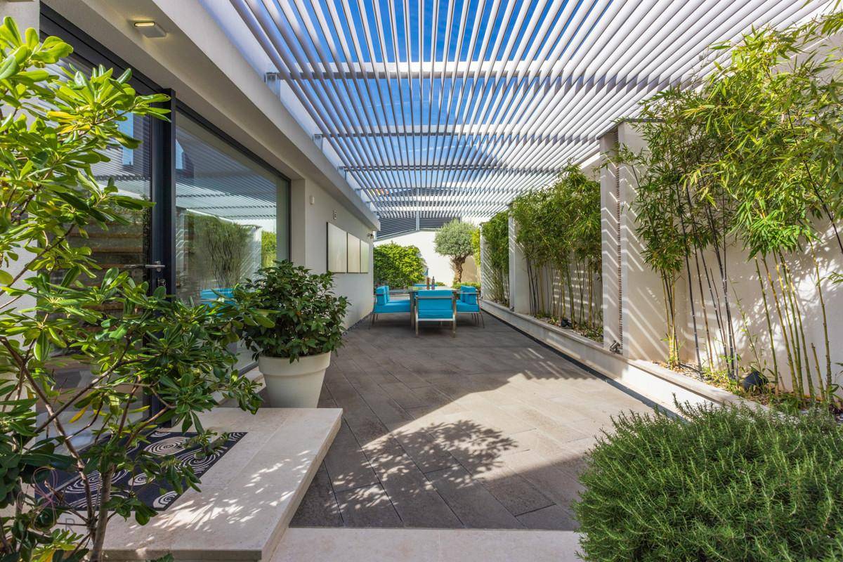 Moderne Terrasse mit Pergola, bequemen Sitzgelegenheiten und üppiger Bepflanzung für entspannte Stunden im Freien.