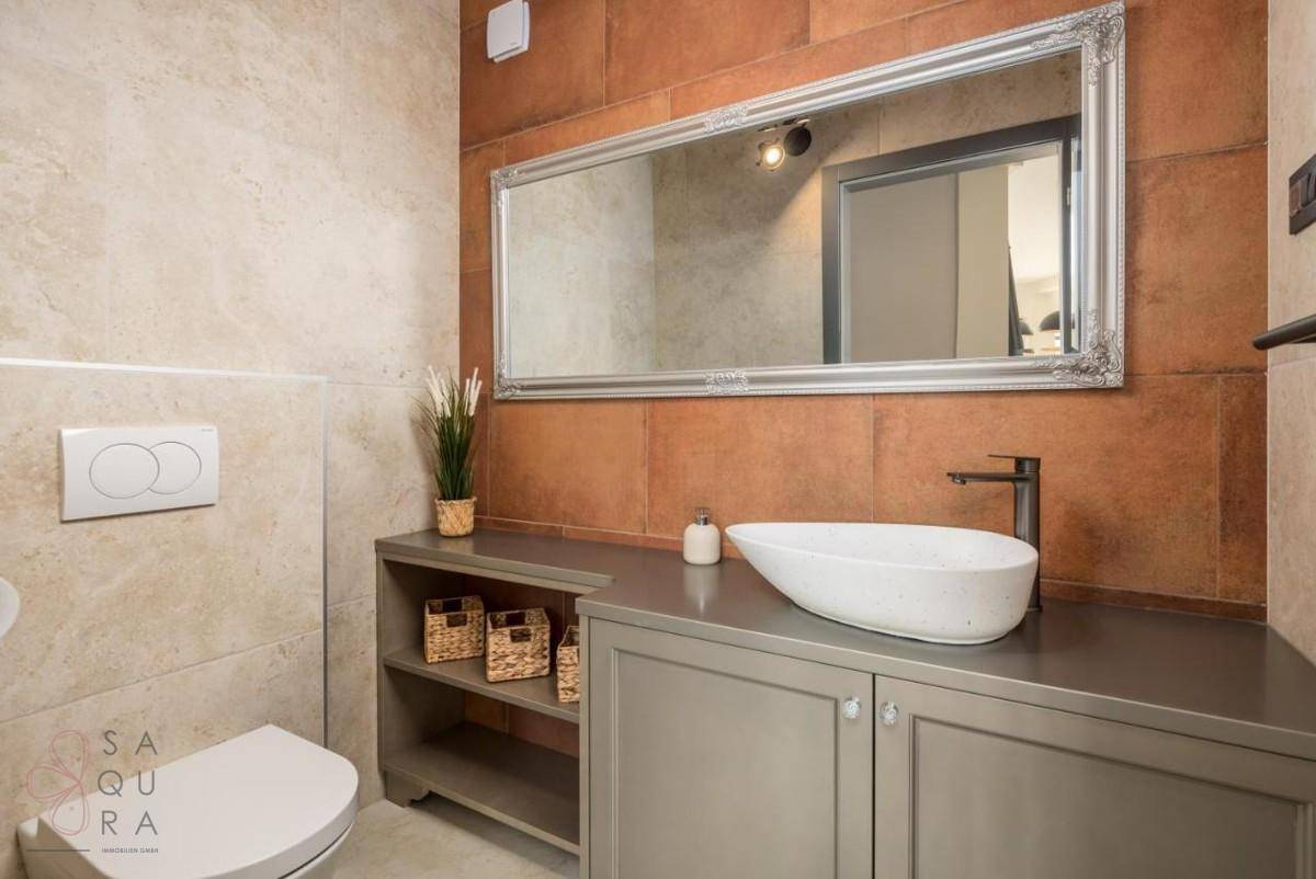 Elegantes Badezimmer mit Aufsatzwaschbecken, Unterschrank und einem großen, verzierten Spiegel über dem Waschtisch.
