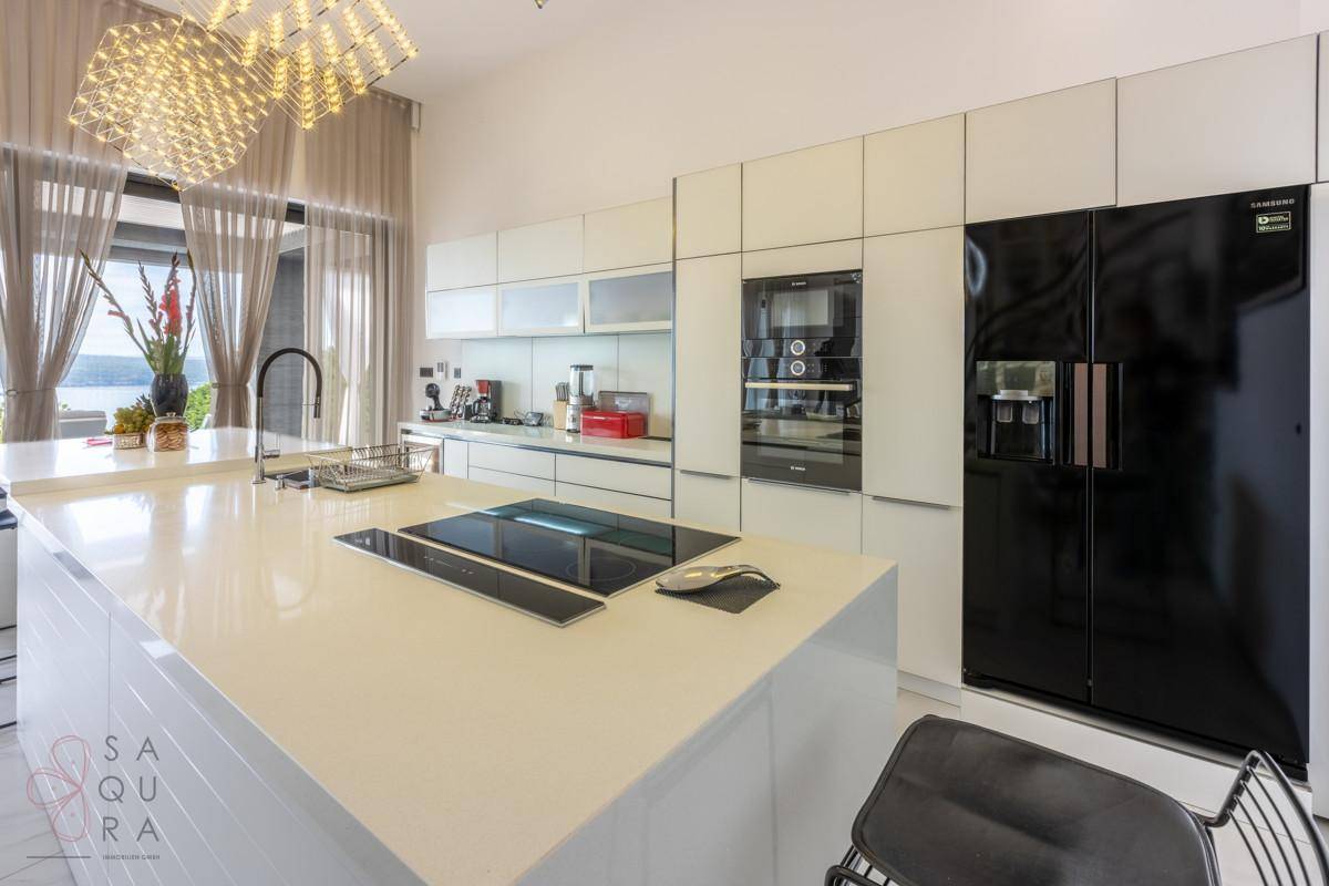 Hochmoderne Küche mit weißen Schränken, integrierten Geräten und großem Kühlschrank.