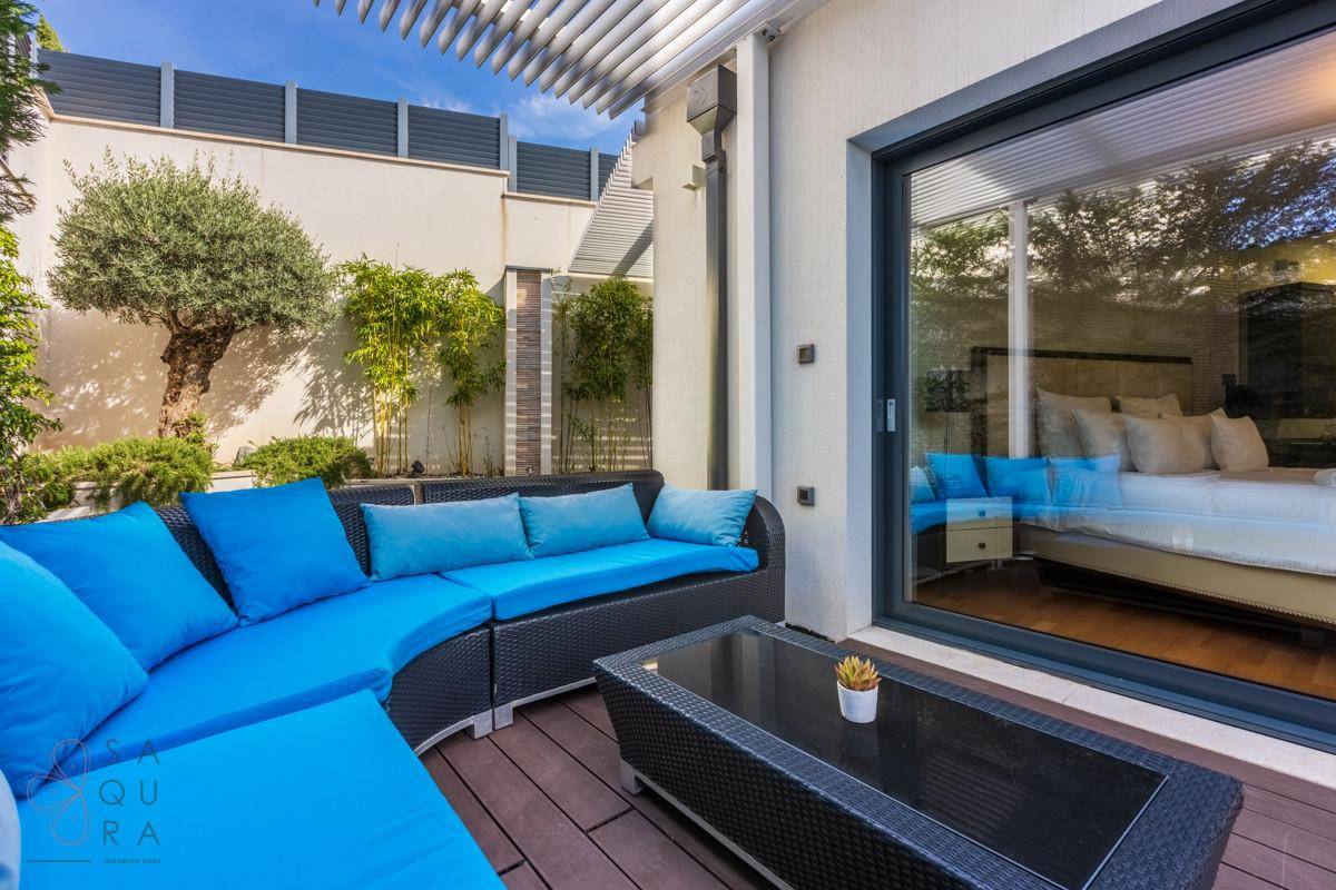 Gemütliche Terrasse mit blauen Lounge-Möbeln und Blick in ein helles Schlafzimmer.