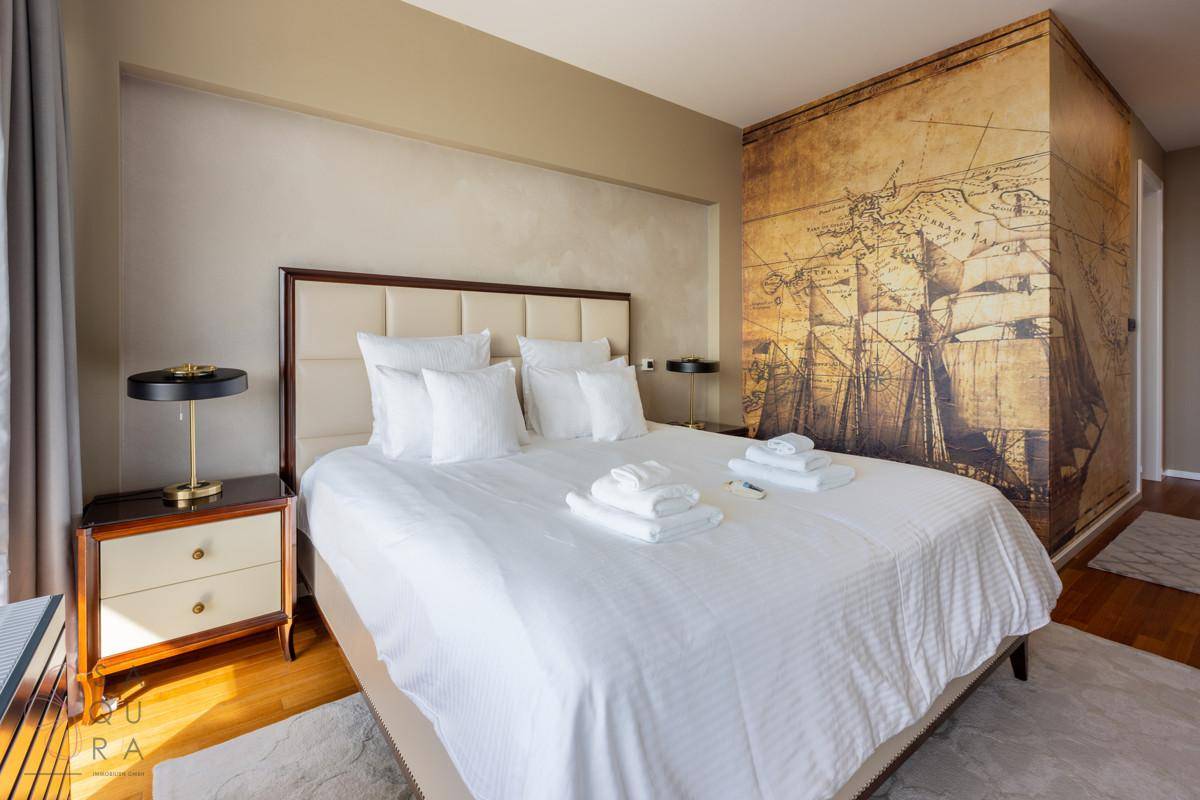 Schlafzimmer mit großem Bett, Holzboden und einer dekorativen Wandtapete mit historischer Seekarte.