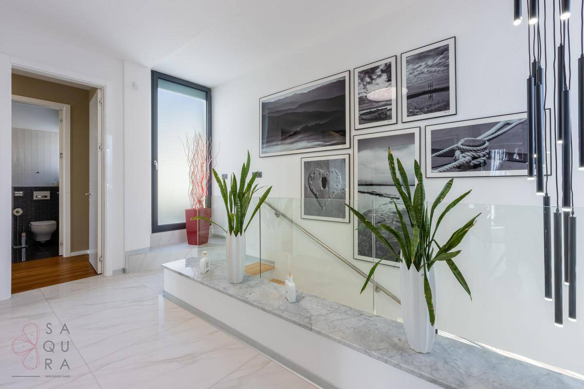 Heller Flur mit Marmorboden, Glasgeländer und moderner Kunst an der Wand.