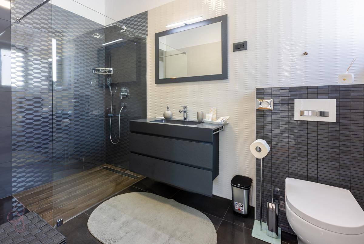 Modernes Badezimmer mit begehbarer Dusche, schwebendem Waschtisch und dunklen Fliesen.
