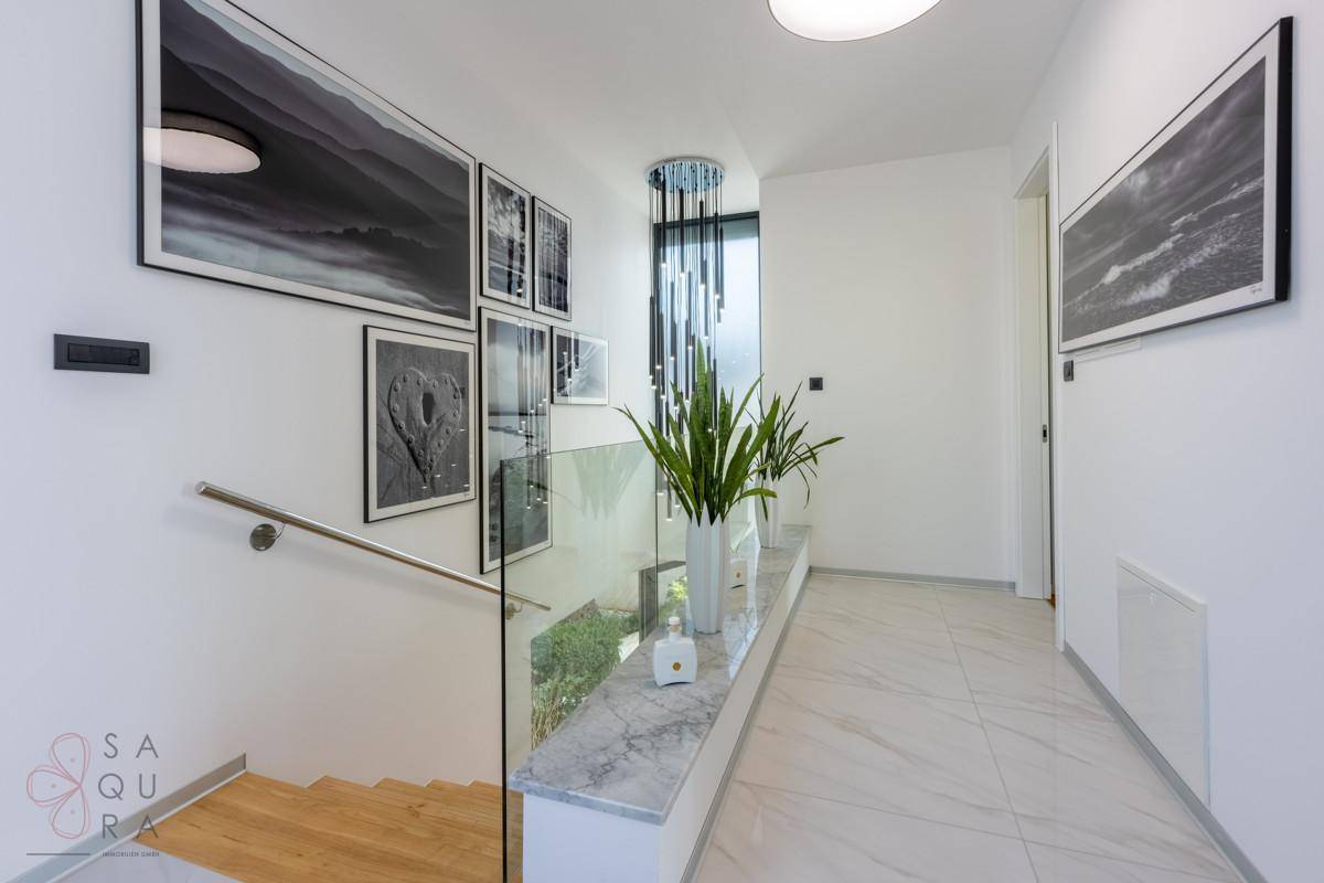 Heller Flur mit moderner Treppe, Glasgeländer und Kunstwerken an den Wänden.