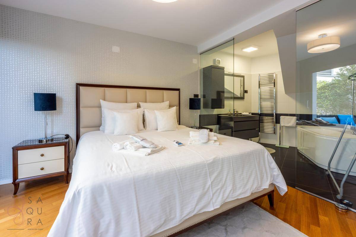 Elegantes Schlafzimmer mit Doppelbett und offenem Zugang zu einem modernen Bad mit Whirlpool.