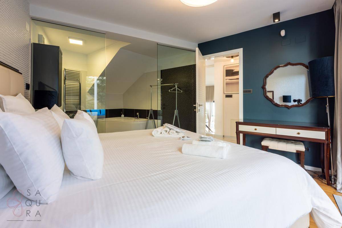 Stilvolles Schlafzimmer mit Holzboden und offenem Übergang zu einem luxuriösen Badezimmer.