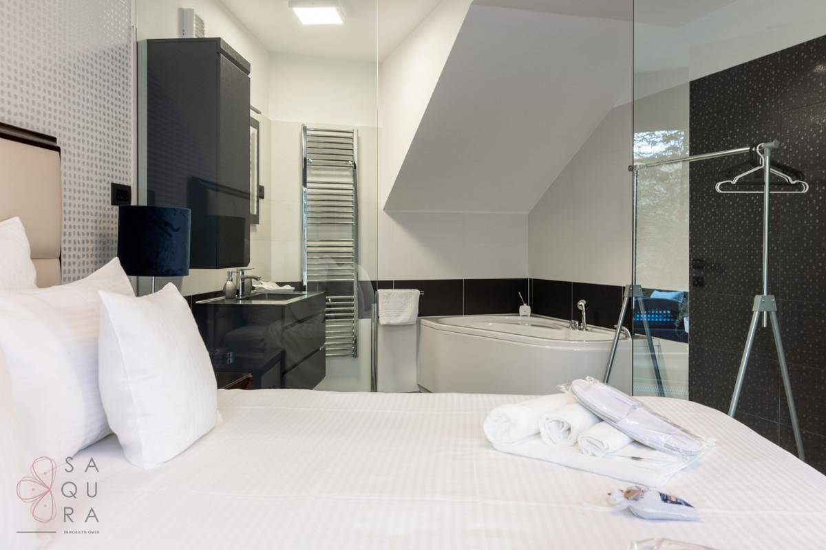 Modernes Badezimmer mit Whirlpool-Badewanne und beheiztem Handtuchhalter, offen zum Schlafzimmer.