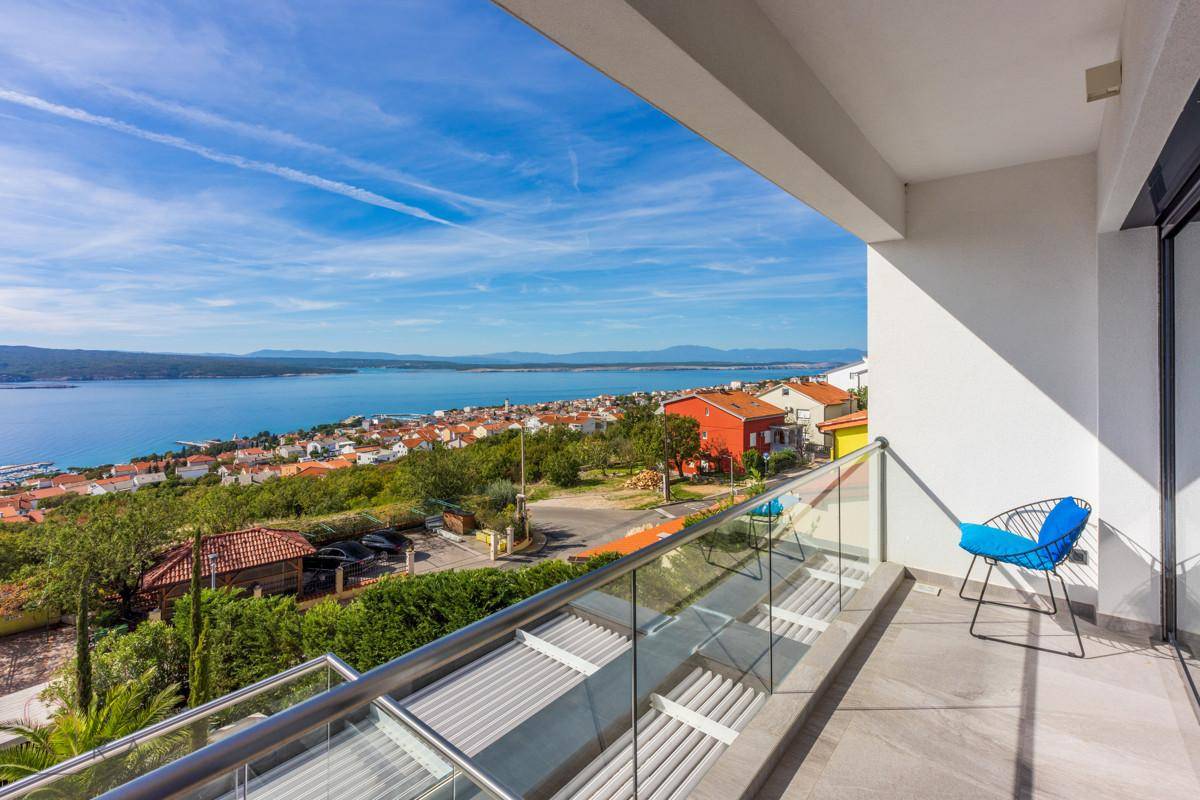 Geräumiger Balkon mit Glasgeländer und atemberaubendem Panoramablick auf das Meer und die Küstenstadt.