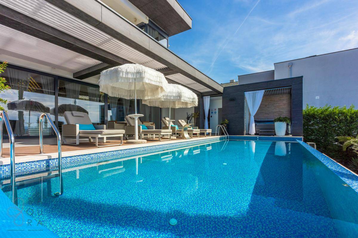 Großer Poolbereich mit Sonnenliegen und einem separaten, überdachten Whirlpool-Bereich.