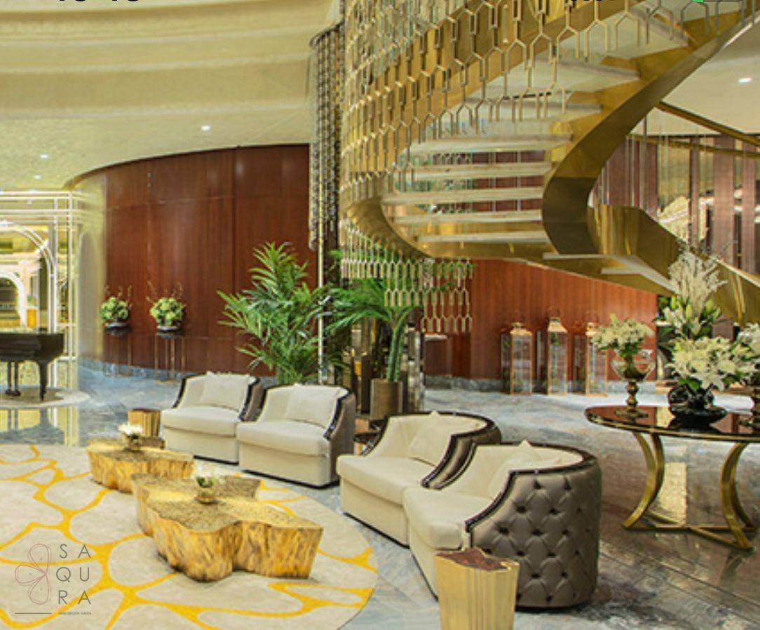 Luxuriöse Hotellobby mit geschwungener Treppe, eleganten Sitzgruppen und Pflanzen.