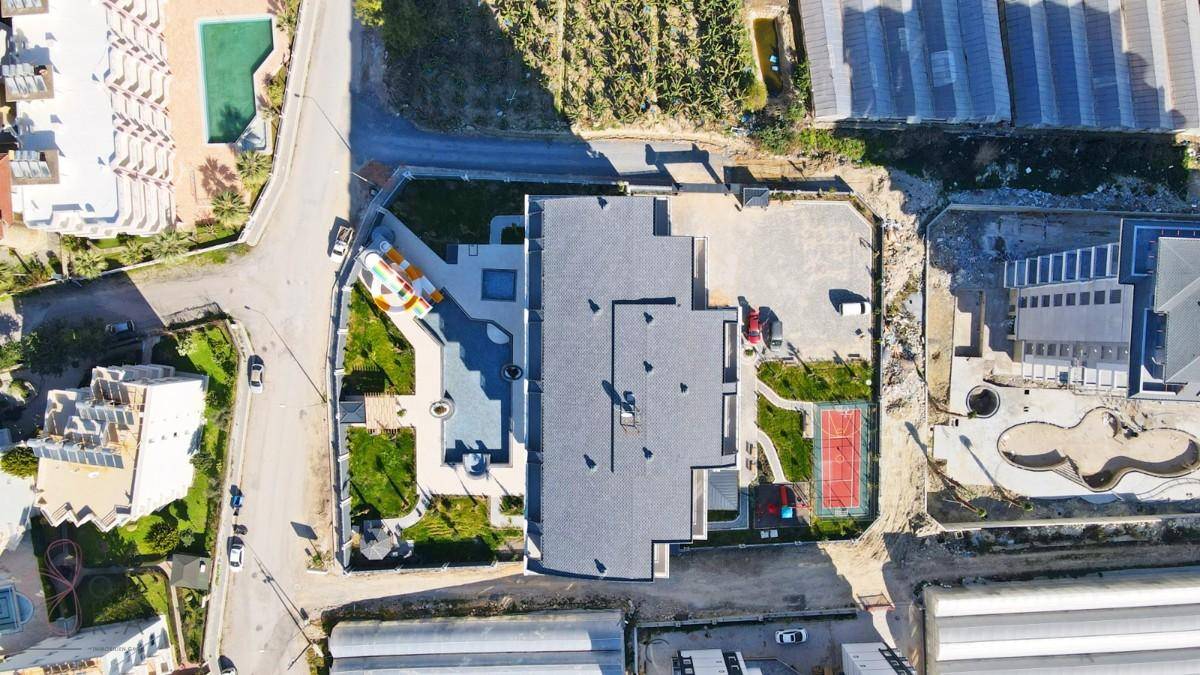 Draufsicht auf das Gebäude mit Flachdach, Poolbereich, Sportplatz und umliegenden Grünflächen.