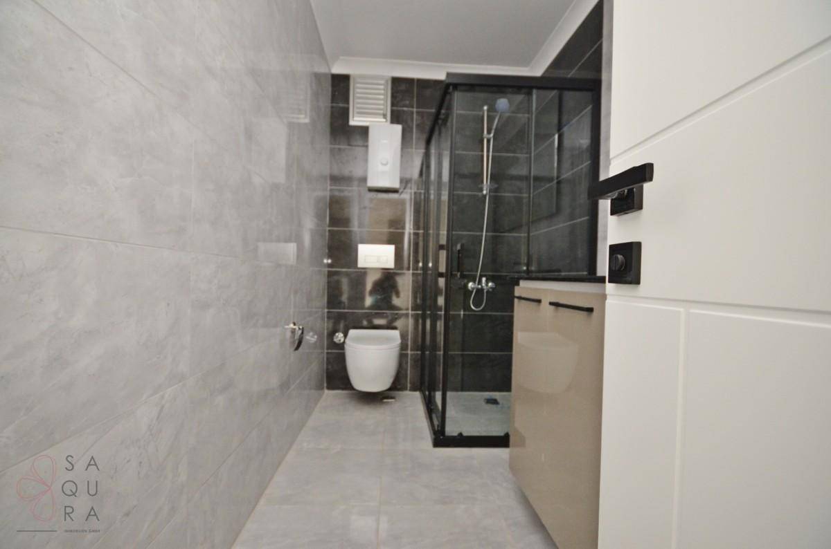 Modernes Badezimmer mit Duschkabine, Wand-WC und hellgrauen sowie dunklen Fliesen.