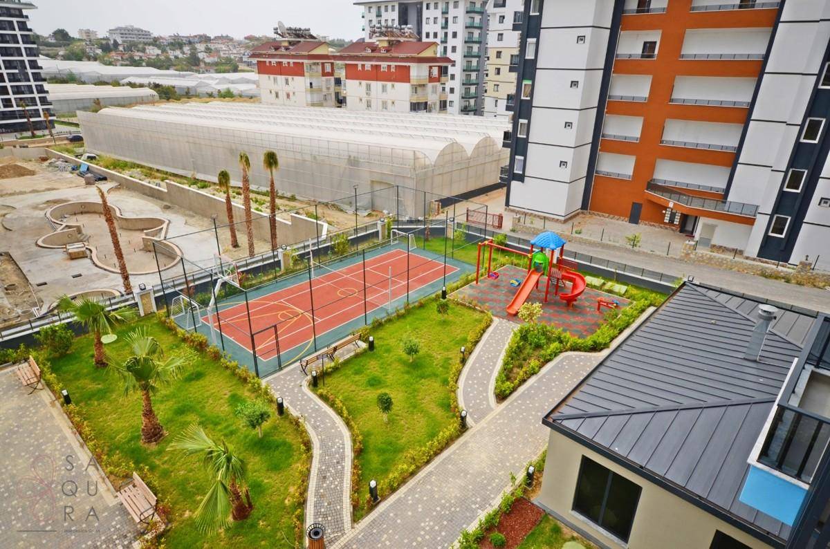 Übersicht über die Freizeitanlagen mit Sportplatz, Kinderspielplatz und Palmen im Wohnkomplex.
