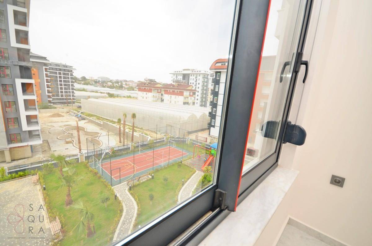 Fensterblick auf die Außenanlagen mit Sportplatz, Spielplatz und Palmen.