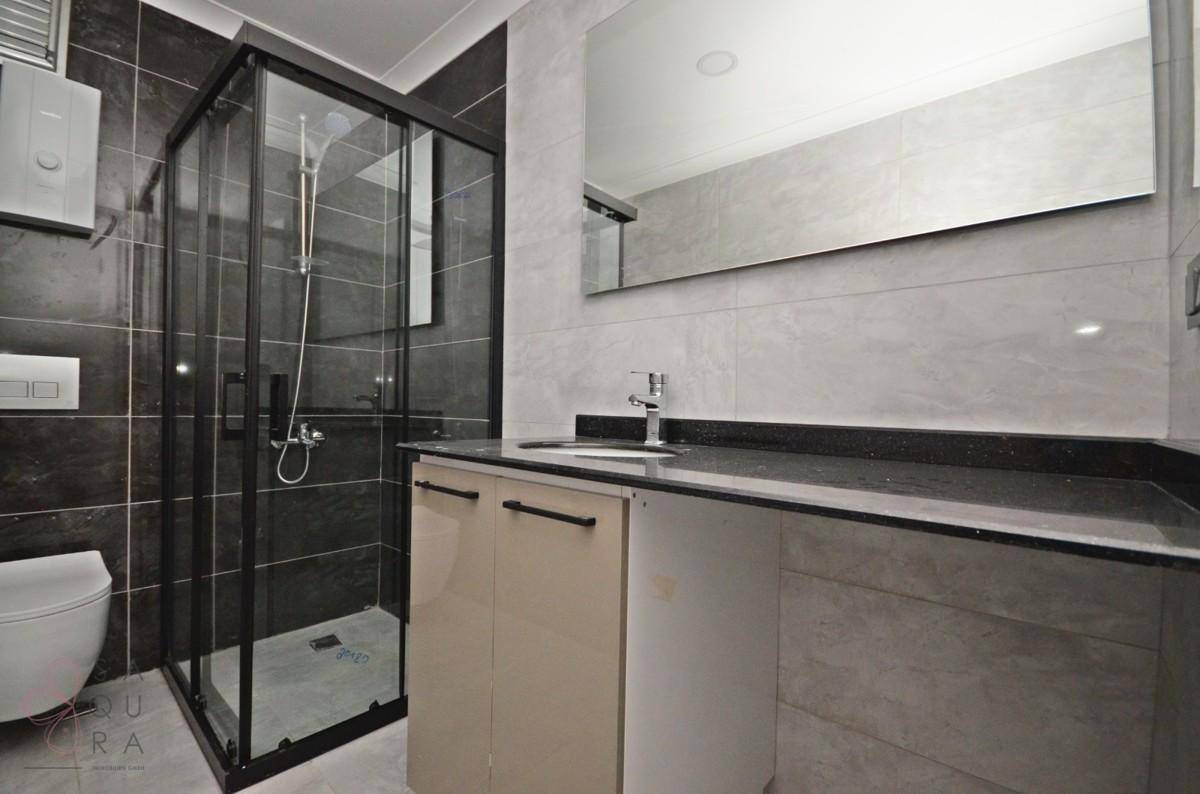 Elegantes Badezimmer mit Duschkabine, Waschtisch und großem Spiegel, in modernen Grautönen gehalten.