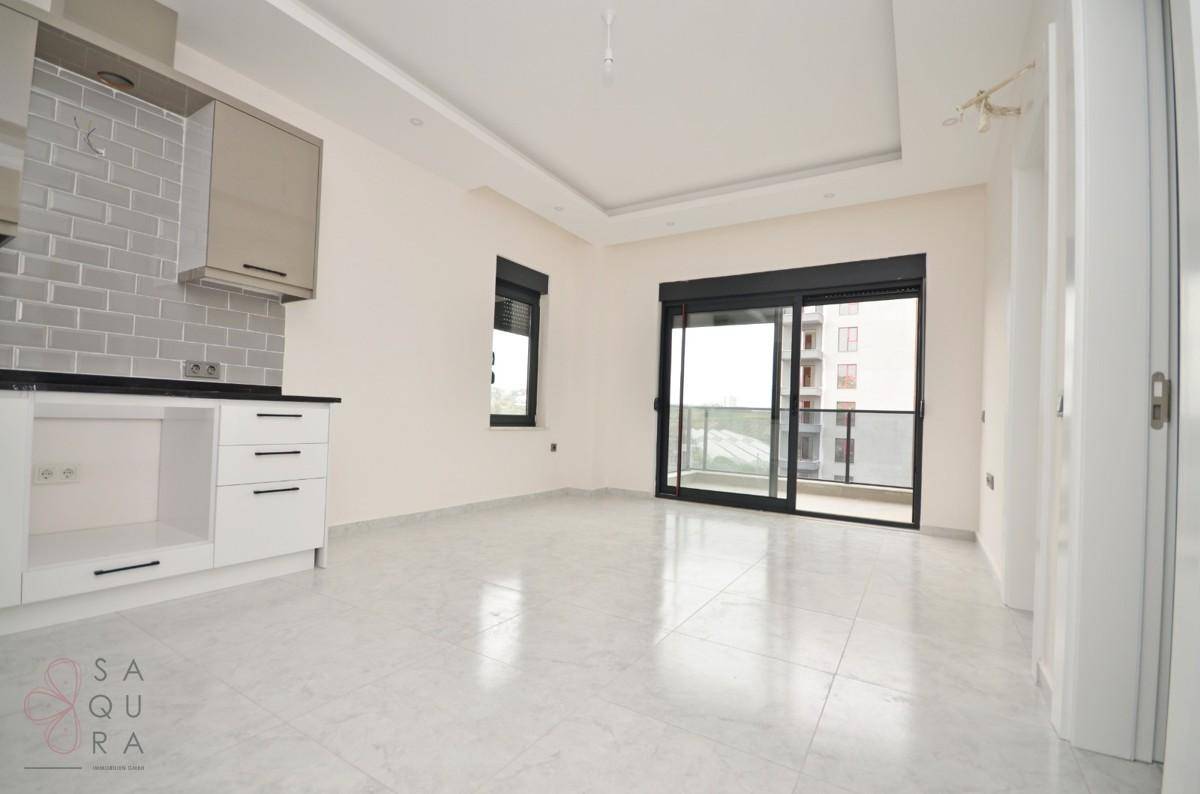 Heller Wohnbereich mit offener Küche, Fliesenboden und Schiebetür zum Balkon.