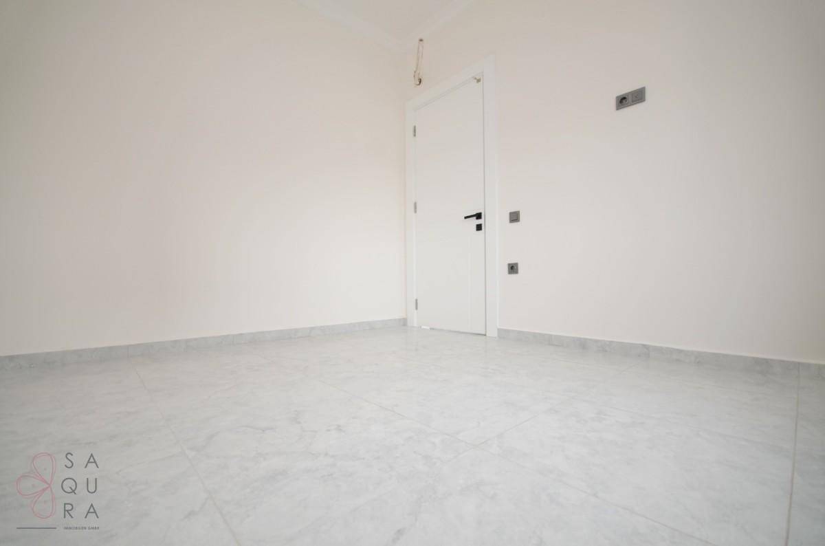 Helles, leeres Zimmer mit Fliesenboden und weiß gestrichenen Wänden, bereit zur Einrichtung.