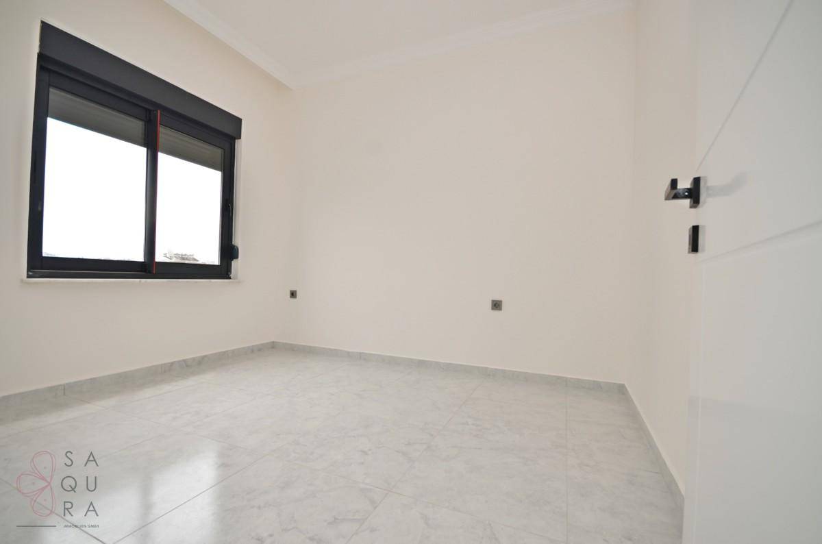Leeres Schlafzimmer mit Fliesenboden, weißen Wänden und einem Fenster mit Rollladen.