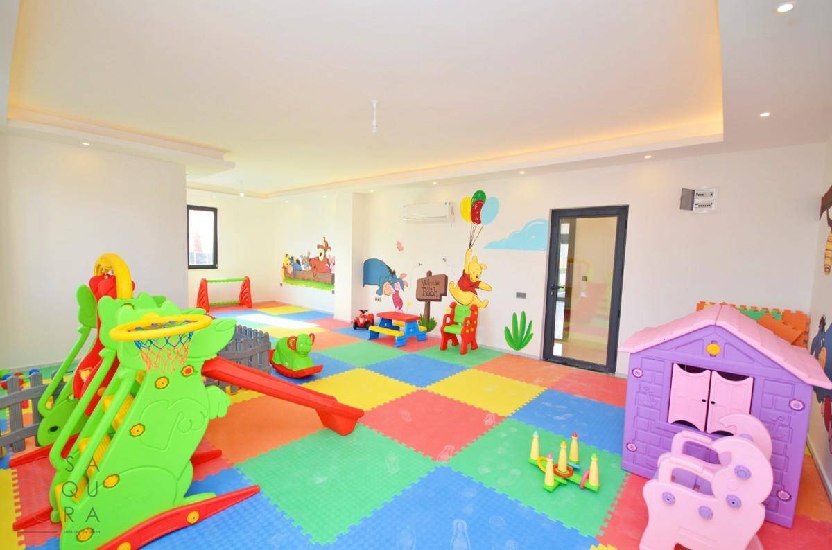 Farbenfroher Kinderspielraum mit weichen Bodenmatten, Rutsche und verschiedenen Spielgeräten.