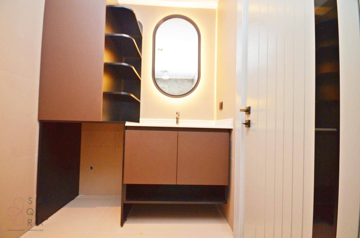 Modernes Badezimmer mit braunem Waschtischunterschrank, ovalem Spiegel und integrierter Beleuchtung.