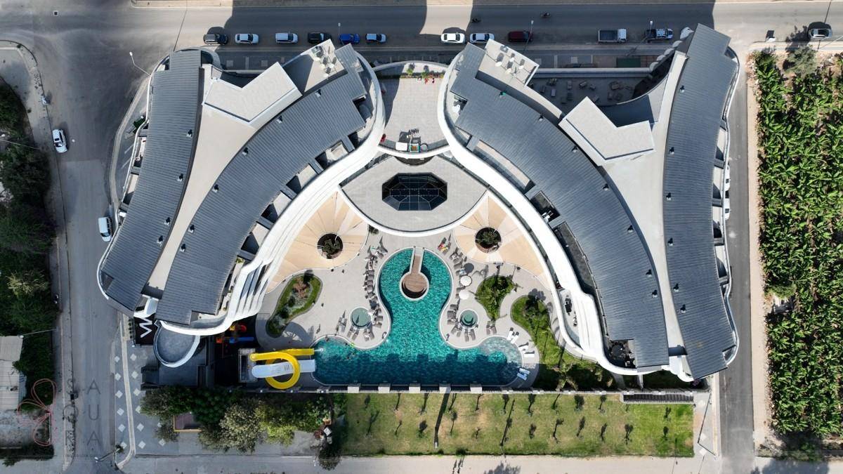 Vogelperspektive des modernen Gebäudekomplexes mit geschwungenen Dächern und zentralem Poolbereich.