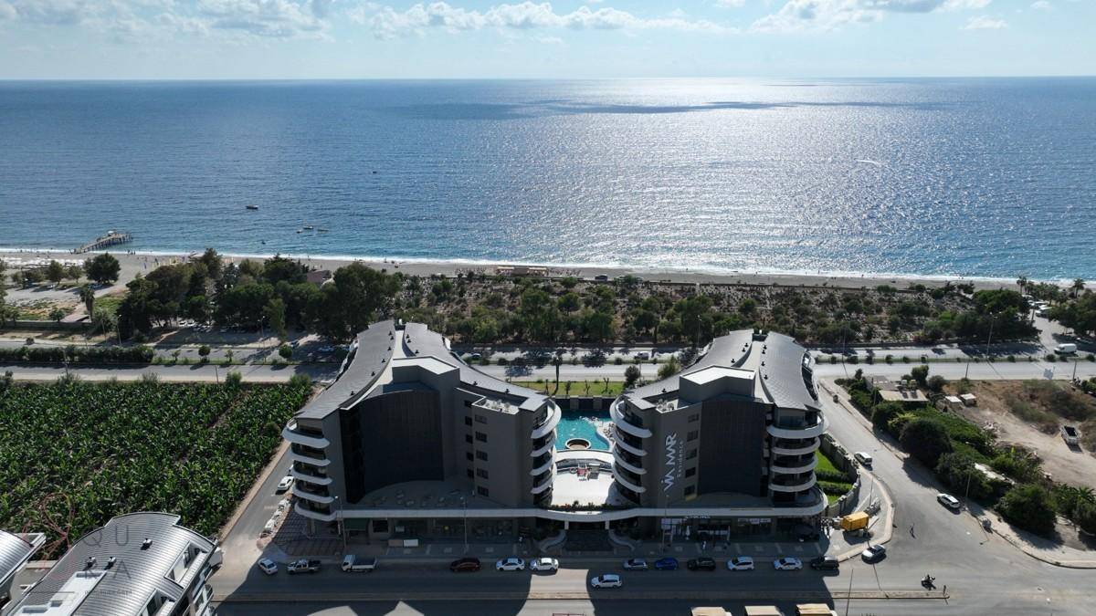 Luftaufnahme des modernen Gebäudekomplexes mit Meerblick und angrenzendem Strandbereich.